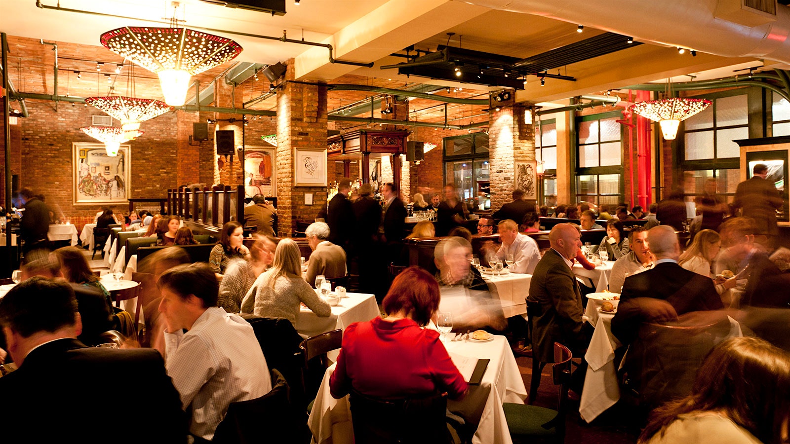 People dining in the Tribeca Grill dining room with contemporary-design lighting fixtures overhead, and bricklined walls and columns throughout